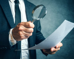 Tax inspector investigating financial documents through magnifying glass forensic accounting or financial forensics inspecting offshore company financial papers documents and reports.